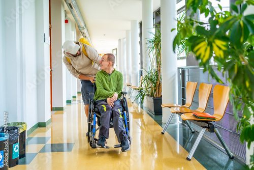 Принти на полотні Friend pushing the wheelchair of a disabled man along university