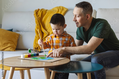 Smiling father teaching son to paint planet earth on cardboard at home photo
