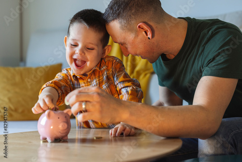 Happy father and son putting coins in piggy bank at home photo
