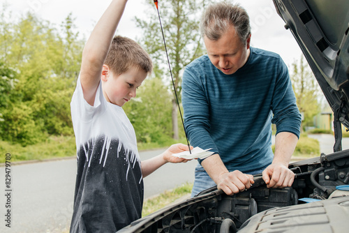 Boy examining dipstick by father leaning on car photo