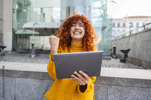 Excited redhead young woman with tablet PC gesturing fist photo