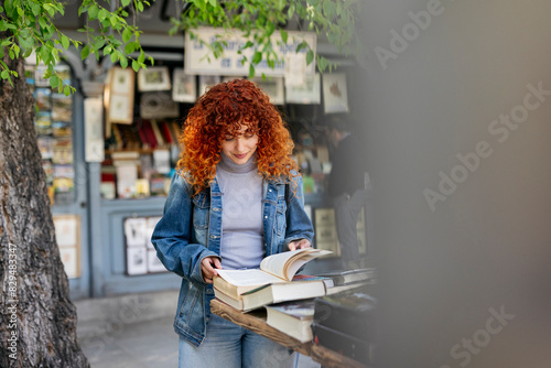 Young redhead woman reading book at market stall photo