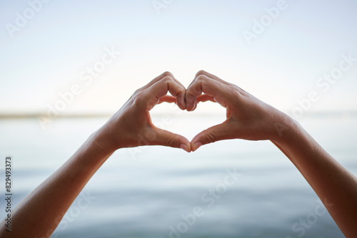 Hands of woman gesturing heart shape in front of lake photo