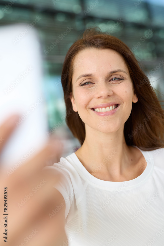 Smiling woman with brown hair taking selfie through smart phone at airport Smiling woman with brown hair taking selfie through smart phone at airport