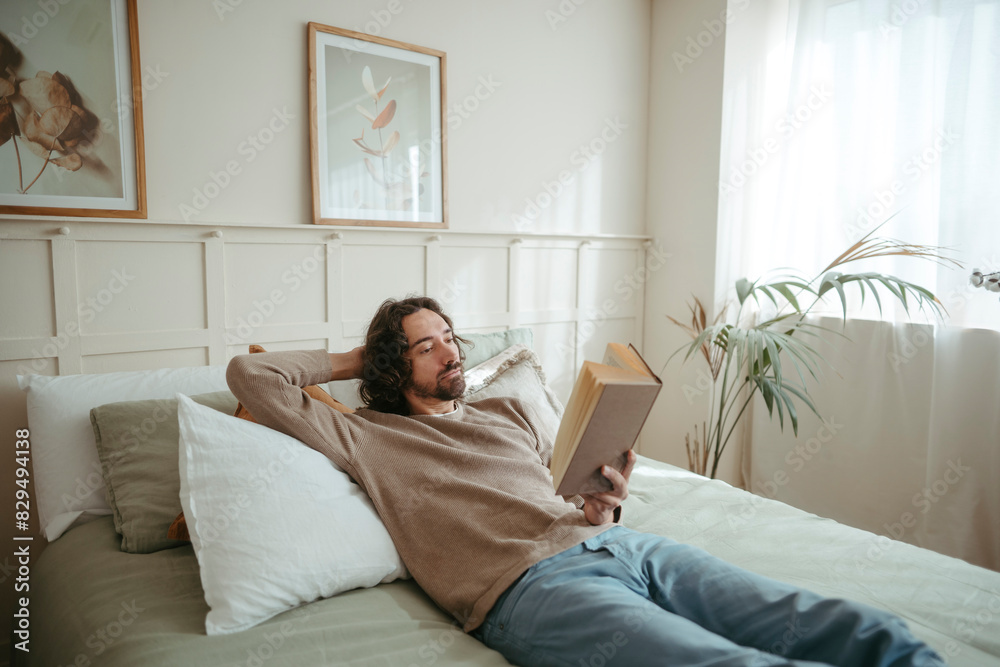 Handsome man reading book lying on bed at home Handsome man reading book lying on bed at home