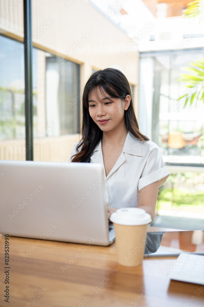 A beautiful Asian businesswoman focusing on her work on a laptop computer in a cafe co-working space A beautiful Asian businesswoman focusing on her work on a laptop computer in a cafe co-working space