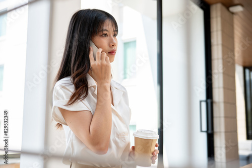 Free Download A confident Asian businesswoman is having a serious phone conversation in the company's corridor. - GFXLoad