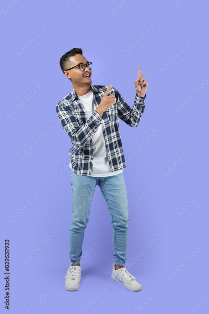 Full-length Portrait of a young Asian man pointing his finger upwards isolated over a purple background while pointing his hand to smartphone Full-length Portrait of a young Asian man pointing his finger upwards isolated over a purple background while pointing his hand to smartphone