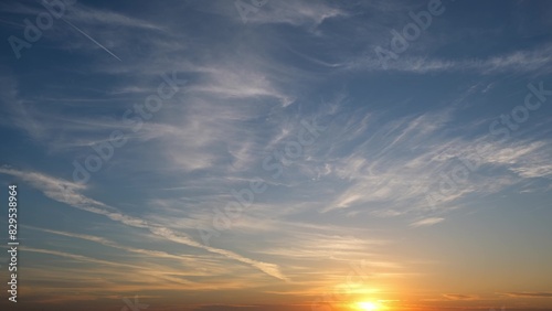 A beautiful sunrise with the sun just above the horizon, casting a warm golden glow. Wispy clouds stretch across the sky, illuminated by the sunlight, creating a serene and peaceful scene. 