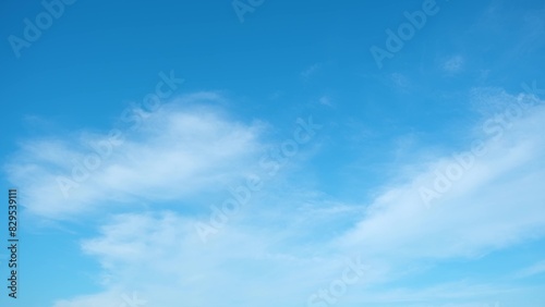 A bright blue sky with a few wispy white clouds scattered across it. The clouds have a soft, fluffy appearance, creating a serene and peaceful atmosphere. Blue sky background.
