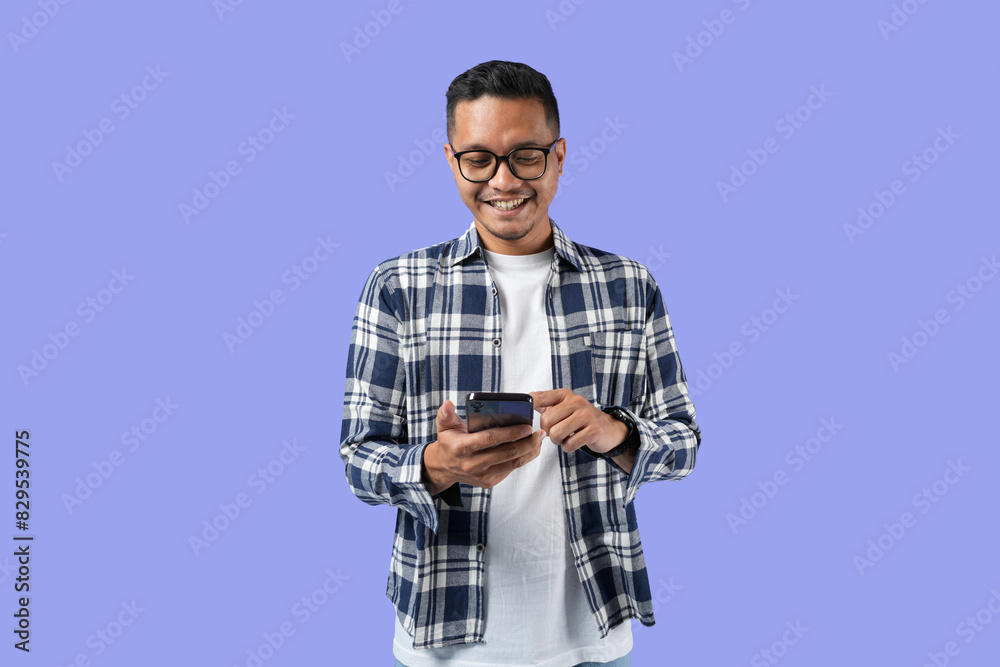 Portrait of a young cheerful excited Asian man standing isolated over a purple background, using a mobile phone Portrait of a young cheerful excited Asian man standing isolated over a purple background, using a mobile phone