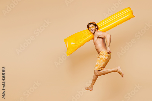 Full body young man wear yellow shorts swimsuit hat relax rest near hotel pool jump high hold inflatable rubber mattress isolated on plain beige background. Summer vacation sea rest sun tan concept.
