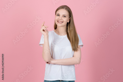 Happy confident caucasian blonde young woman in casual white t-shirt standing looking at camera isolated on pink studio background. Smiling, friendly and successful.