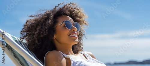 An upbeat young African American woman in sunglasses enjoys a carefree vacation while sunbathing on a deck chair by the sea creating a copy space image