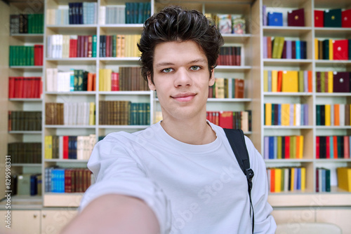 Selfie portrait of smiling college student guy inside library of educational building