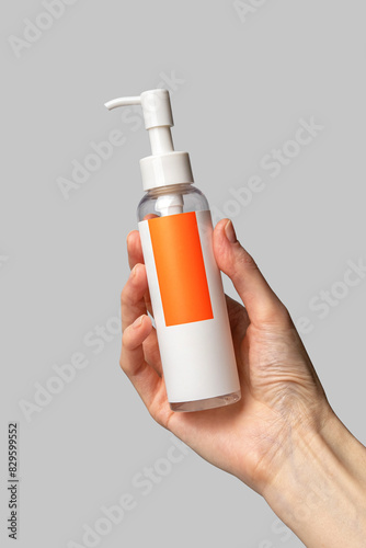 Woman hand showing hydrophilic face oil. Cosmetic product branding mockup. Daily skincare and body care routine. Female hand holding  cosmetic product mockup on a light gray background. Close up.