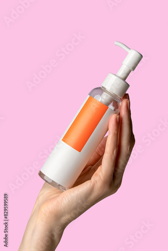 Woman hand showing hydrophilic face oil. Cosmetic product branding mockup. Daily skincare and body care routine. Female hand holding  cosmetic product mockup on a light pink background. Close up.