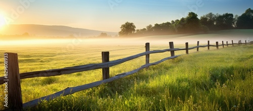 Fototapeta Naklejka Na Ścianę i Meble -  Morning light illuminates a rural farm fence with a copy space image of farmland and wild grass in the background