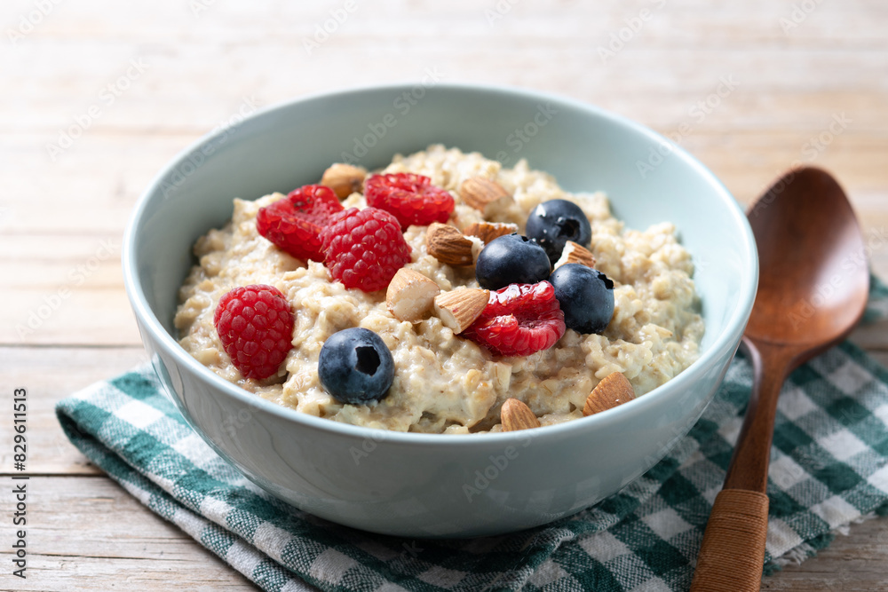 Oatmeal porridge with raspberries, blueberries and almonds in bowl on wooden table Oatmeal porridge with raspberries, blueberries and almonds in bowl on wooden table