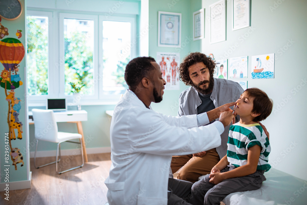 Pediatrician giving a young boy an oral vaccine with his father watching Pediatrician giving a young boy an oral vaccine with his father watching