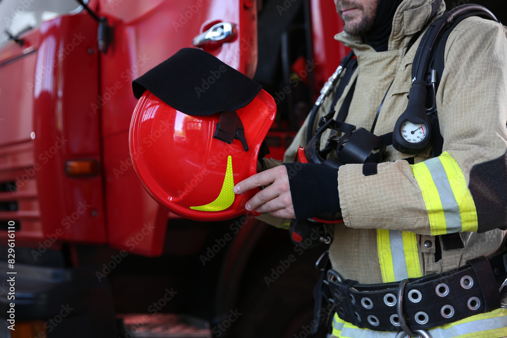Firefighter in uniform with helmet near red fire truck at station, closeup Firefighter in uniform with helmet near red fire truck at station, closeup