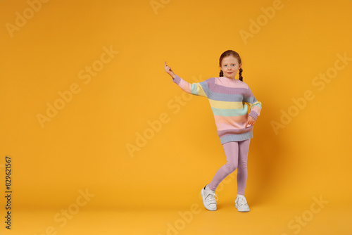 Cute little girl dancing on orange background, space for text