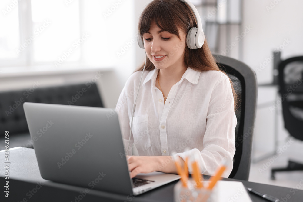 Woman in headphones watching webinar at table in office Woman in headphones watching webinar at table in office