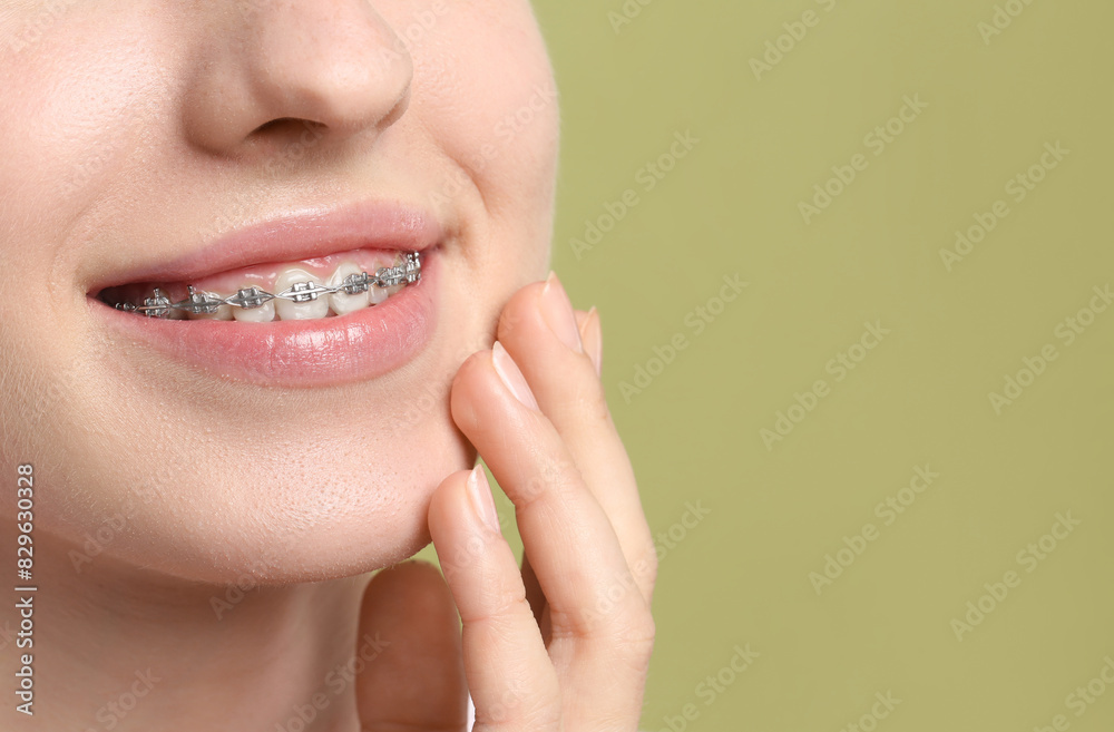 Obraz premium Smiling woman with dental braces on light green background, closeup. Space for text