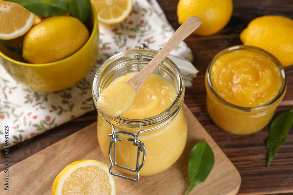 Delicious lemon curd in glass jars, spoon, fresh citrus fruits and green leaves on wooden table Delicious lemon curd in glass jars, spoon, fresh citrus fruits and green leaves on wooden table