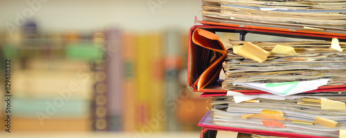 stack of messy file folders with narrow depth of field, blurred bookshelf  in the back,red tape, bureaucracy,aministration,business concept.