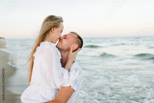 Love. Couple hugging and kissing on seashore in sea. Male kisses and hugs female standing on water with big waves ocean and enjoying a summer day. Man embraces woman walking on beach sand sea. photo