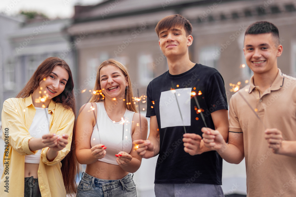 Obraz premium Two cute guys and two charming girls are holding sparklers and smiling