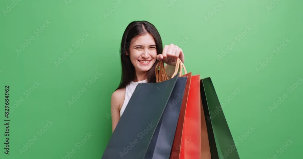 Cheerful young woman holding shopping bags. Isolated on green background in studio.