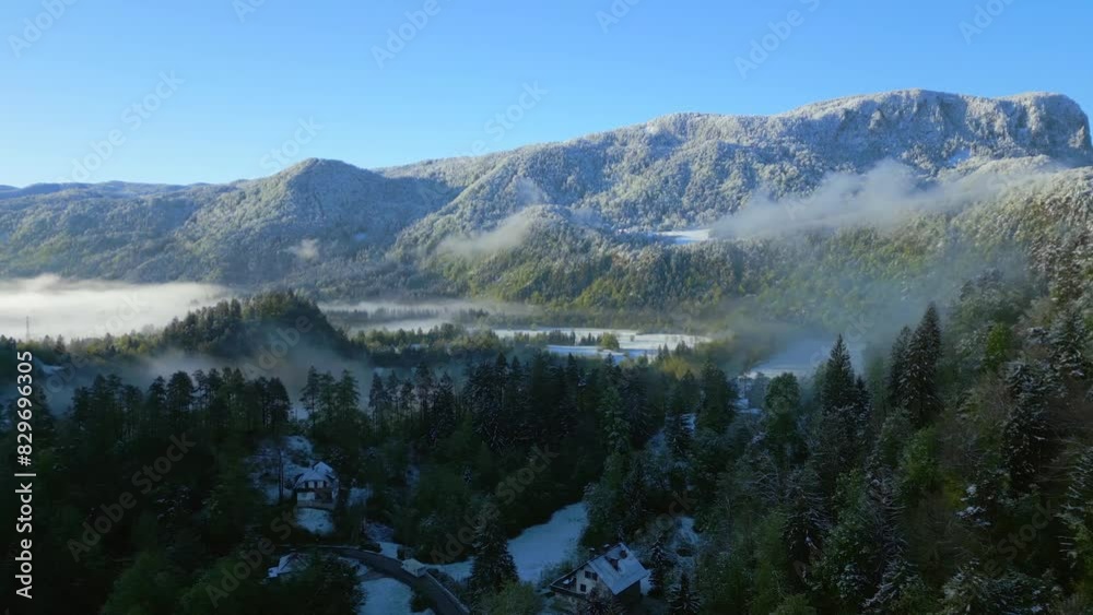 Aerial breathtaking view of a snow-capped mountain towering over a mist-enshrouded forest and valley Aerial breathtaking view of a snow-capped mountain towering over a mist-enshrouded forest and valley