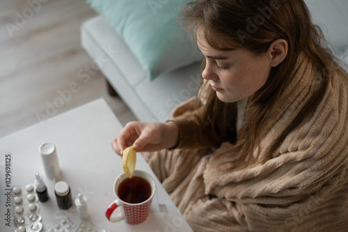 sick woman holding slice of lemon over cup of hot tea. treatment of flu, colds. photo