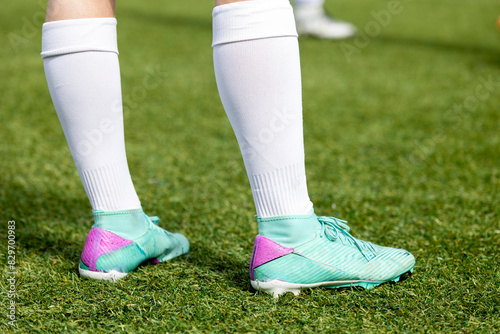 A partial view of a soccer player standing on a grass field with a focus on the legs and soccer cleats