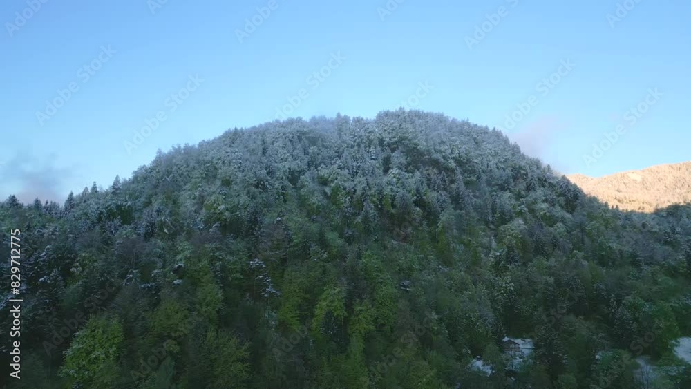 Snow-capped forested hill under a clear sky, marking a seasonal transition from winter to spring. Snow-capped forested hill under a clear sky, marking a seasonal transition from winter to spring.