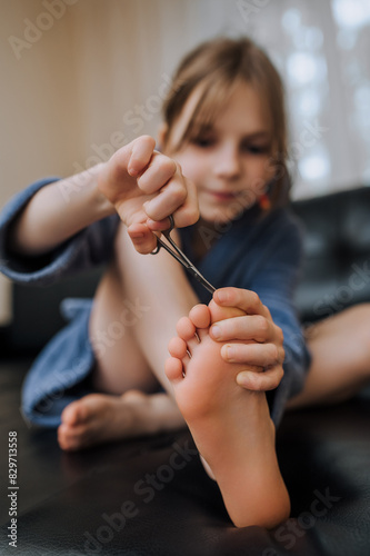 Girl, child sitting in the room on the sofa, cutting her toenails with manicure scissors. Close-up photography, cosmetic procedure, self care concept.