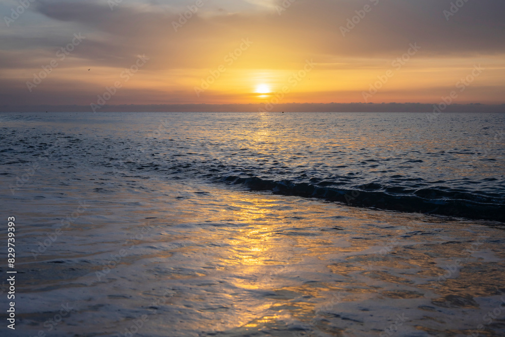 The sunset over the sea, with the sky tinged with gold and the light reflecting on the waters.