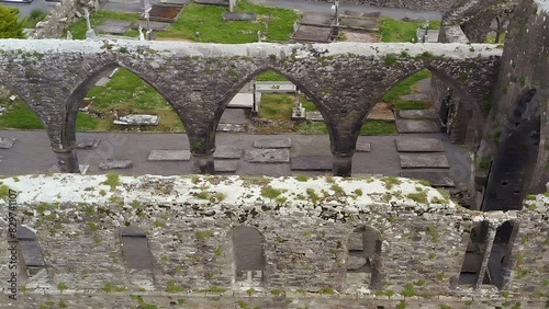 High stone arches of crumbling ruins in Claregalway Friary covered with moss, aerial high angle pan photo
