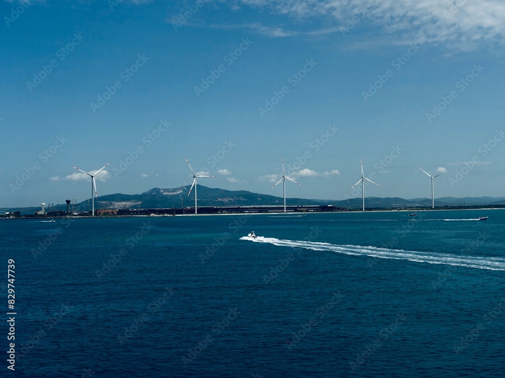 Fototapeta premium Boats sailing past windmills in the ocean beneath a clear blue sky