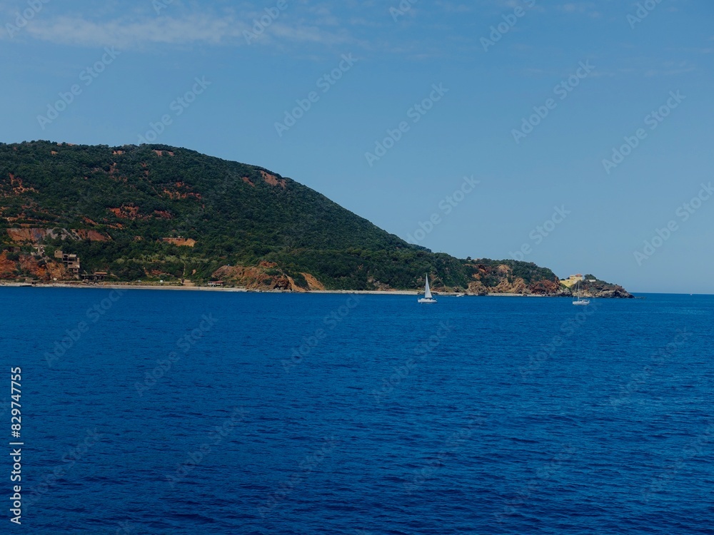 Boat sailing in the ocean with hills, buildings, and coastline in the background Boat sailing in the ocean with hills, buildings, and coastline in the background