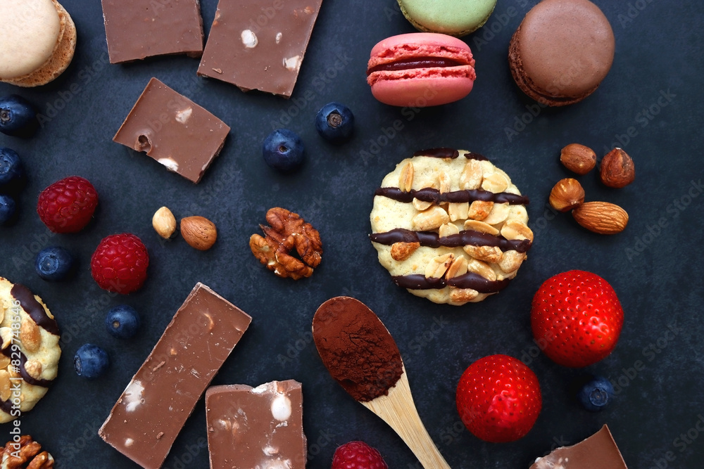 Macarons, chocolate, cookies, berries and various nuts on dark blue background. Top view. Macarons, chocolate, cookies, berries and various nuts on dark blue background. Top view.