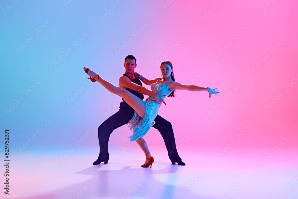 Portrait of young talented couple practicing ballroom dancing in motion in neon lighting against gradient background. Concept of dance and music, professional sport, action, competition, classical. Ad