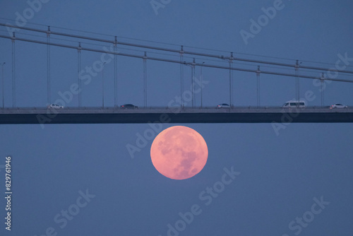 Full moon over Bosphorus bridge at night. The bright and full moon dominates the sky, casting a serene glow over the scene. Perfect for themes related to astronomy, lunar phases, and celestial events. photo