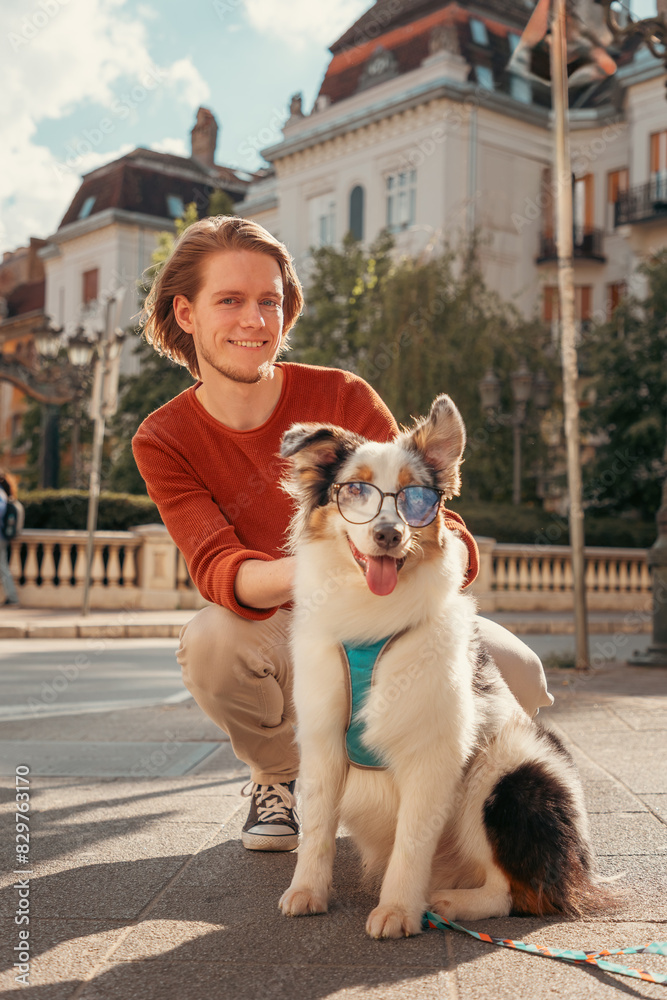 Young Caucasian bearded man walking in old city with purebred Aussie dog. Vertical orientation. Pet training and friendship with dog