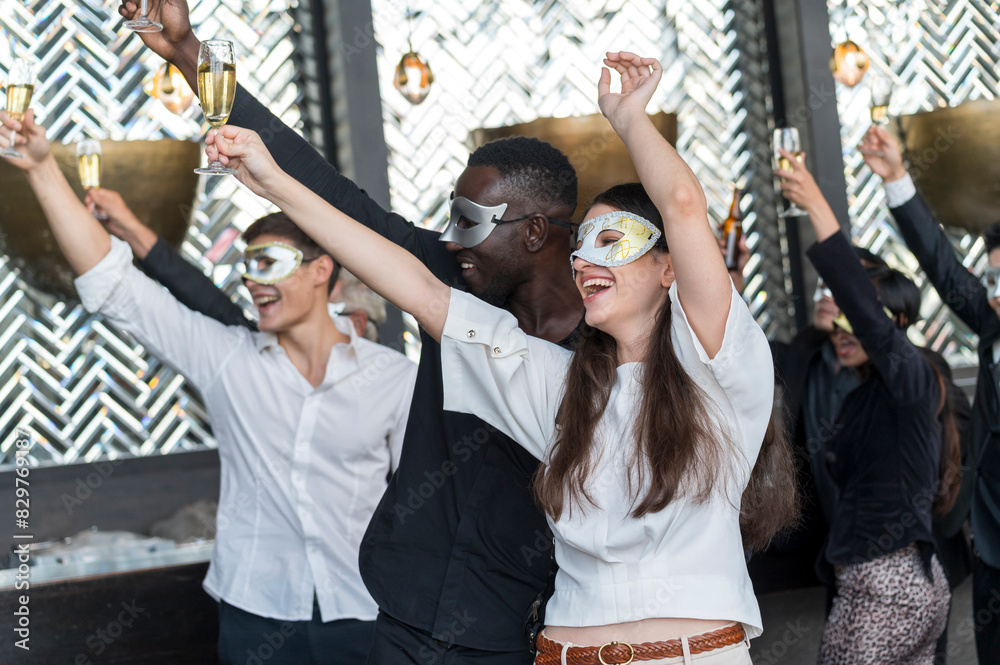 Obraz premium Group of diverse friends toasting with clinking champagne glasses at funny and happy Christmas and new year mask party atmosphere. Holiday celebrate and nightlife lifestyle concept