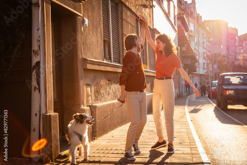 Romantic date of man and woman dancing on the street. Man and woman walking with dog Aussie. Sunset light in background
