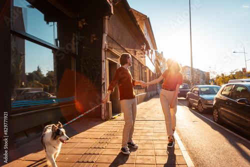 Happy couple walking on the street with purebred dog Aussie. Pet training. Friendship with pet. Sunset light in background