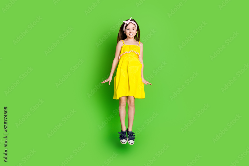 Full length photo of girlish pretty little lady dressed yellow outfit jumping high smiling empty space isolated green color background Full length photo of girlish pretty little lady dressed yellow outfit jumping high smiling empty space isolated green color background